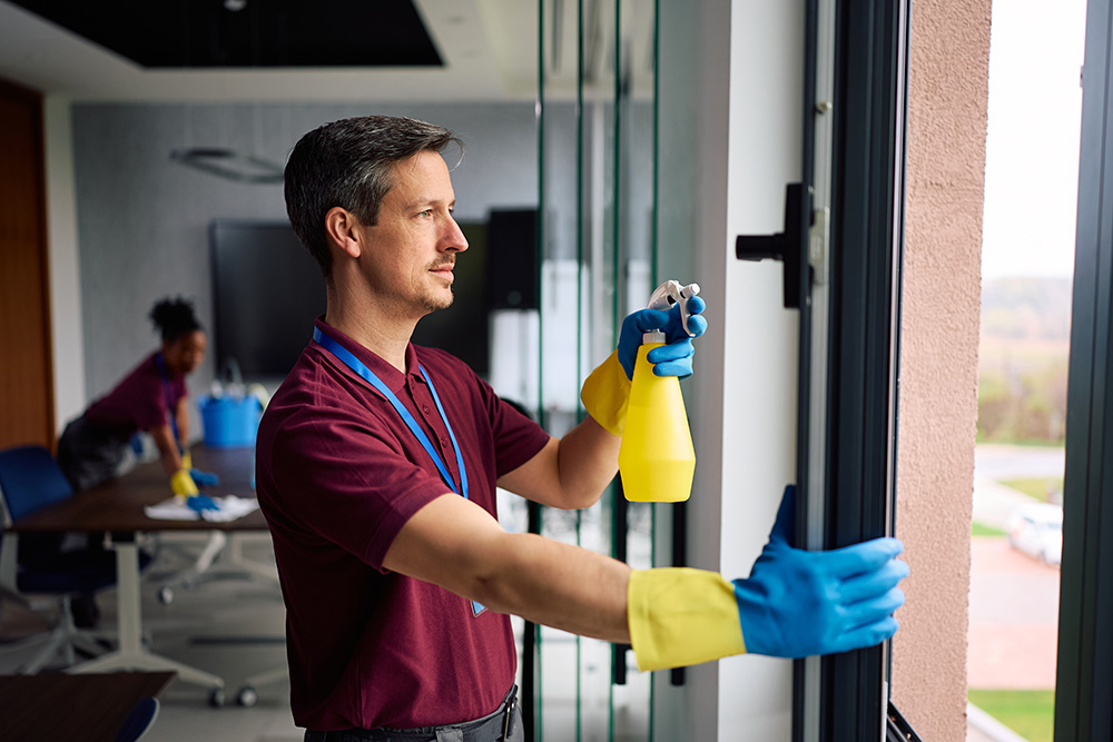 Commercial cleaning professional wiping down modern office windows for MMM Cleaning in Dearborn.