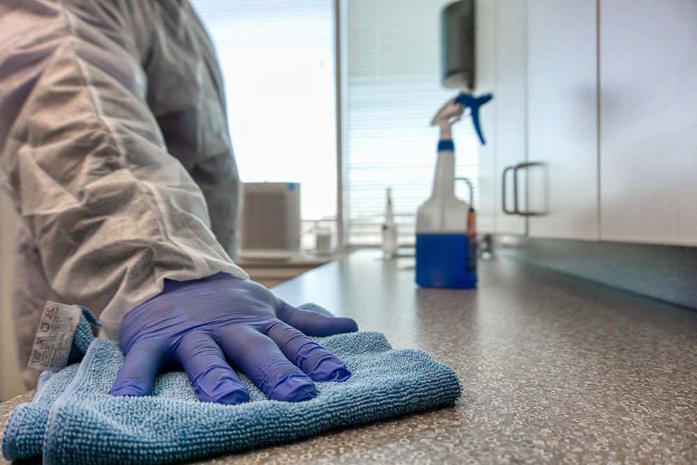 Commercial sanitation worker in protective suit wiping down office countertops in Detroit.