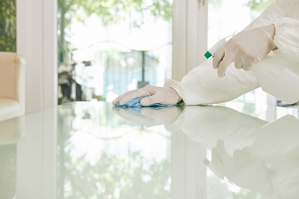 Sanitizing technician in full suit wiping down a reflective glass table in a Farmington Hills commercial office.